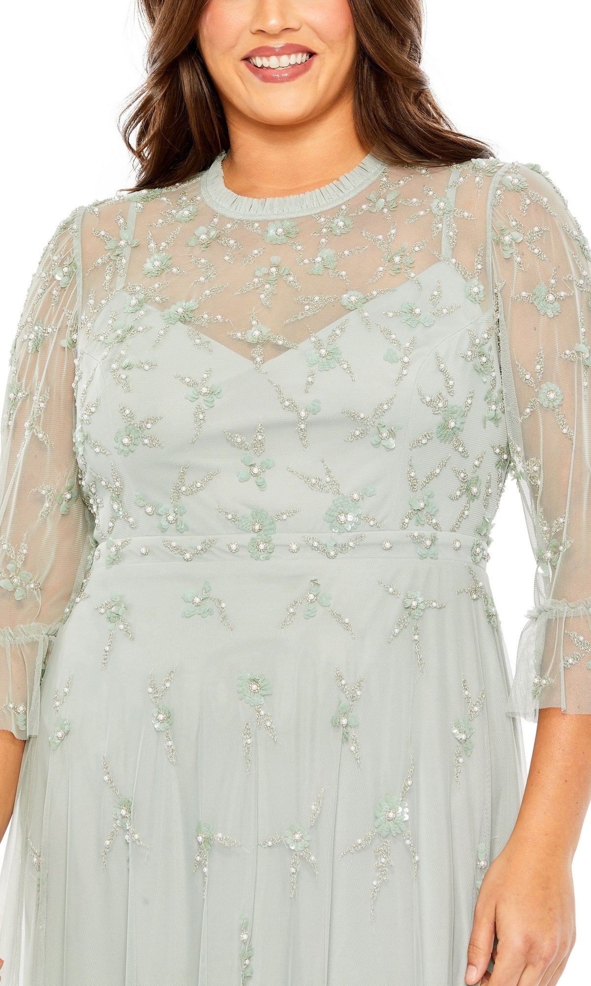 Woman modeling the Mac Duggal Tea-Length Plus-Size Formal Dress 9263—light green, with sheer sleeves, floral embroidery, and sequin accents—smiles against a white background.